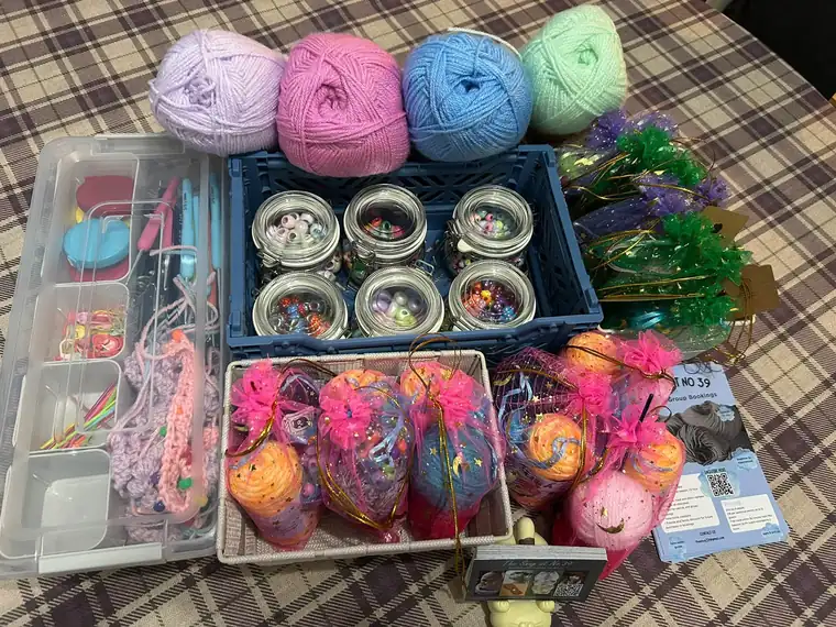 Class kits laid out on a table: balls of pastel yarn, jars of stitch markers and wrapped beginner packs