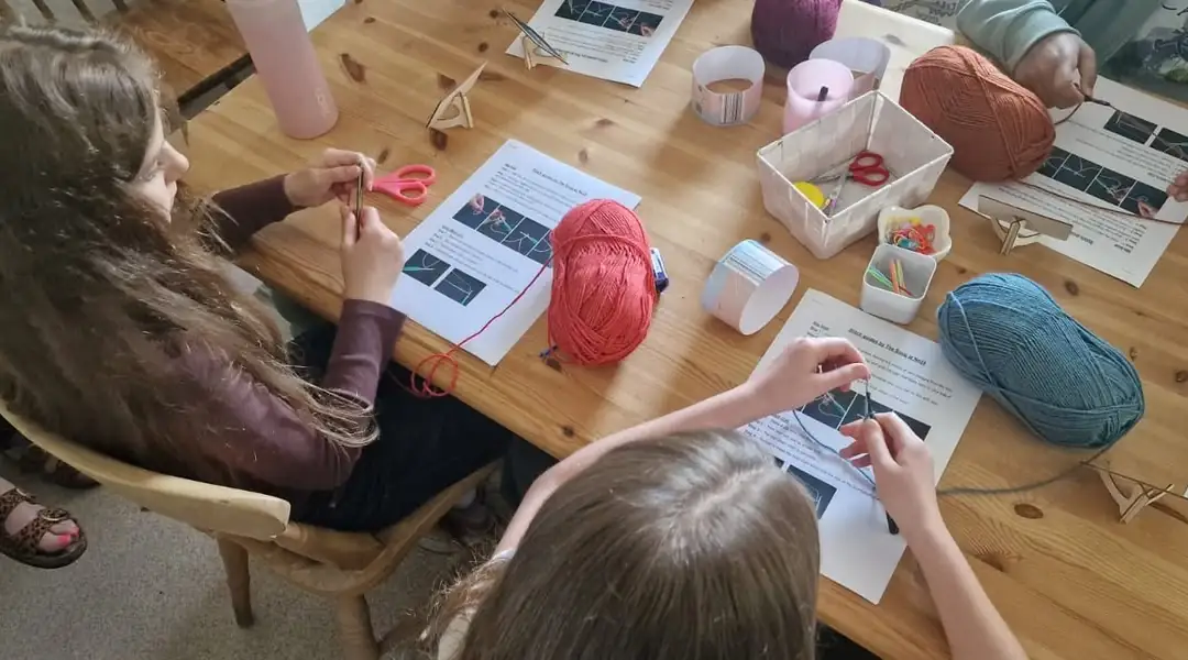 Children learning to crochet around a table with balls of yarn and step-by-step stitch guides