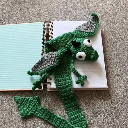 Green crochet dragon bookmark with wings, draped over a notebook