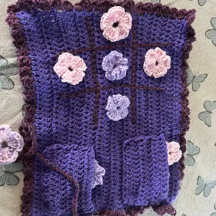 A purple crochet noughts and crosses board with flower counters in contrasting colours