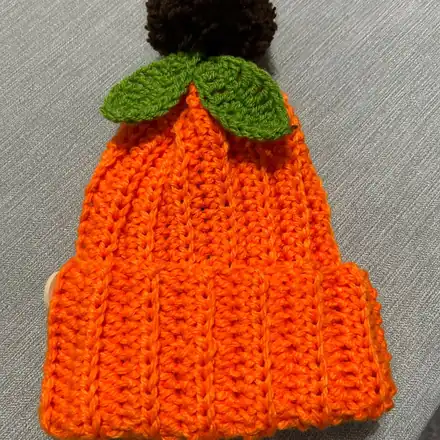 Orange pumpkin hat with a brown pom-pom and green leaves