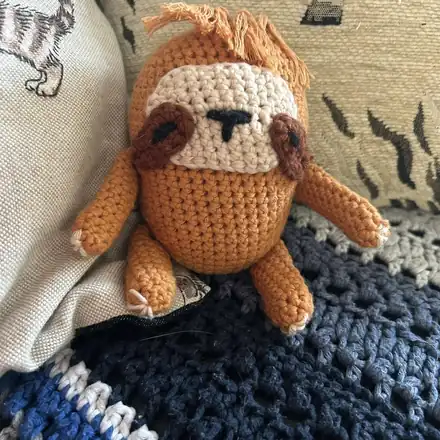 Crochet sloth toy sitting on a blanket